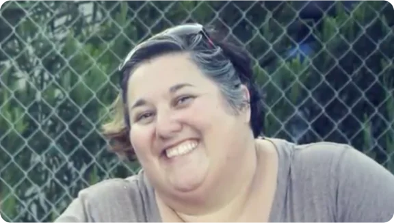 a person smiling in front of a chain link fence
